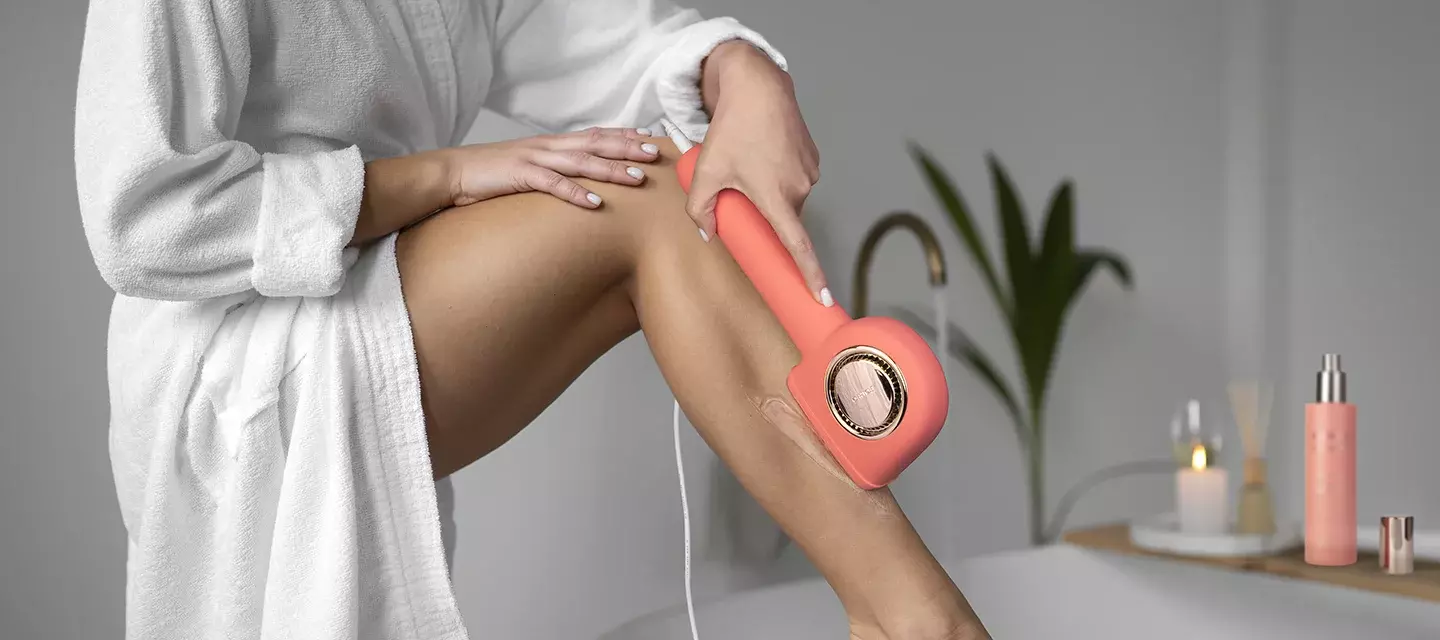 hair removal at home A woman with beautiful legs in white robe doing IPl hair removal at home in a beautiful space